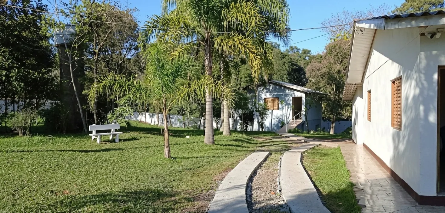 Área externa com gramado, palmeiras, banco e caminho até as casas da unidade